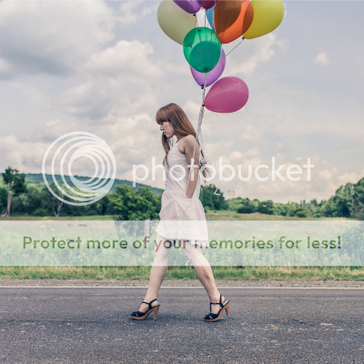 A woman walking down a country road holding multicoloured balloons